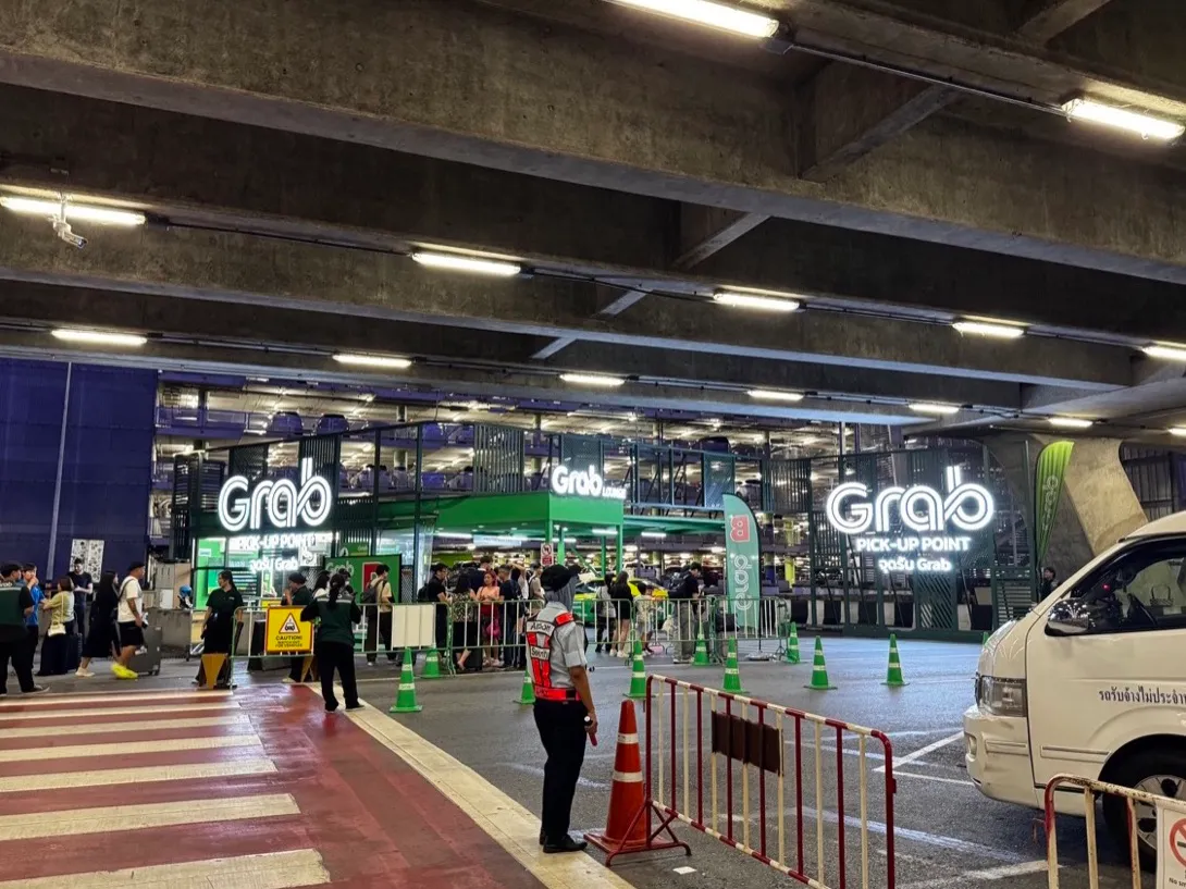 Подсвеченная зелёная точка подачи Grab в аэропорту Суварнабхуми с буквенными зонами ожидания и сотрудниками в зелёном